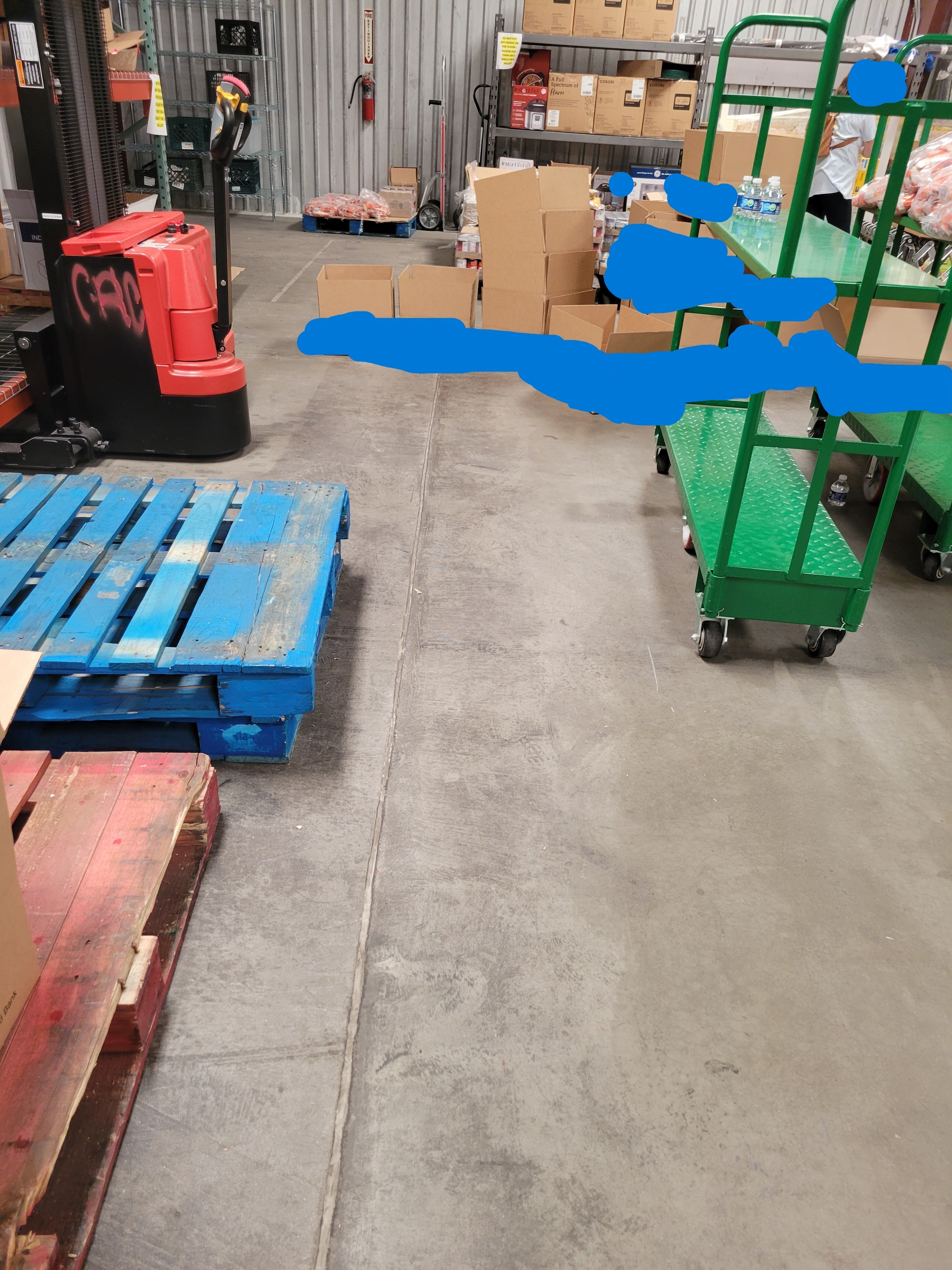Two pallets, shelf cart, and pallet stacker near each other with boxes behind it.